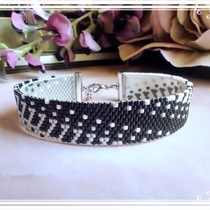 May include: A black and white beaded bracelet with a geometric pattern. The bracelet has a silver clasp.