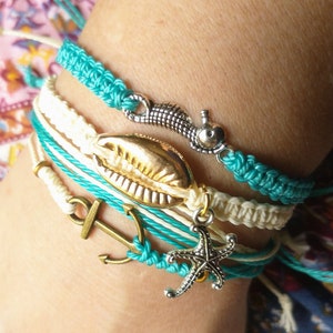May include: A set of four bracelets with nautical themes. The bracelets are made of white and turquoise cord and feature a gold seashell charm, a silver seahorse charm, a silver anchor charm, and a silver starfish charm.