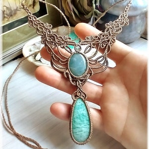 May include: A green gemstone necklace with a brown cord and intricate macrame knotwork. The necklace features two large teardrop-shaped gemstones and a smaller round gemstone.
