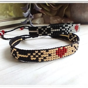 May include: Two beaded bracelets with black, white, gray, and red beads. The bracelets have a geometric pattern and a red heart design.