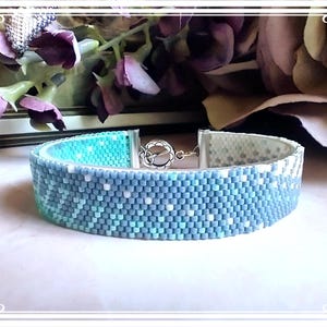 May include: A blue and white beaded bracelet with a silver clasp. The bracelet is made with small, square beads in a geometric pattern.