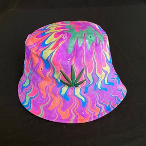 May include: A pink, blue, green, and yellow tie-dye bucket hat with a green marijuana leaf embroidered on the front.