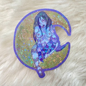 May include: A holographic sticker featuring a woman with long black hair sitting on a crescent moon. The moon is surrounded by stars and has a purple outline. The woman is wearing a blue and white striped outfit and has a tattoo of a crab on her chest.
