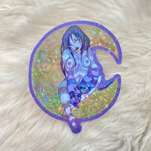 May include: A holographic sticker featuring a blue-toned illustration of a woman sitting on a crescent moon with stars. The woman is wearing a striped outfit and has long dark hair. The sticker has a purple border.