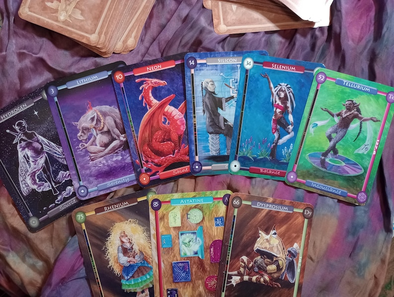 Pu&ograve; includere: Un set di carte da gioco colorate con illustrazioni di creature mitiche ed elementi. Le carte sono numerate con i numeri atomici di diversi elementi, come l'idrogeno, il neon, il litio, il silicio, il selenio, il tellurio, il renio, l'astato e il disprosio.