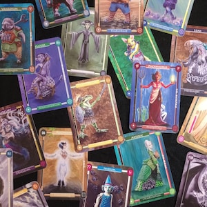 Pu&ograve; includere: Un set di carte da gioco colorate con creature fantastiche ed elementi. Ogni carta ha un'illustrazione e un testo unici, tra cui nomi come "Vanadium", "Polonium" e "Iridium".