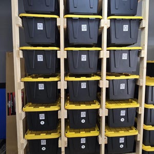 May include: A wooden storage rack with multiple black bins with yellow lids. The bins are arranged in rows and columns, and some are labeled with numbers. The rack has wheels for easy movement.