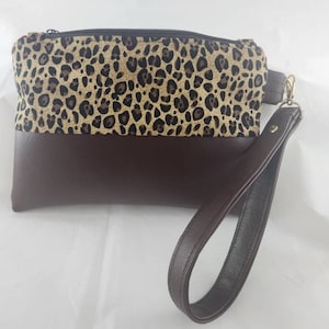 May include: A brown and tan leopard print clutch purse with a brown leather strap.