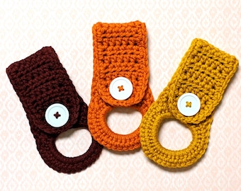 May include: Three crocheted towel holders in brown, orange, and yellow with white buttons. The holders are made with a simple stitch pattern and have a ring at the top for hanging.  Etsy.com/shop/maeakathryn