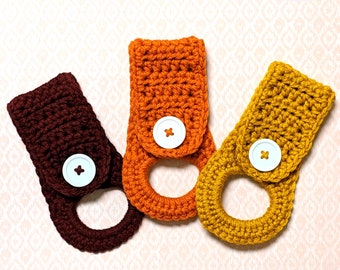 May include: Three crocheted towel holders in brown, orange, and yellow with white buttons. The towel holders are made with a simple stitch pattern and have a loop for hanging.