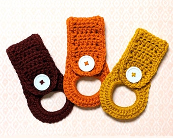 May include: Three crocheted towel holders in brown, orange, and yellow with white buttons. The holders are made with a simple stitch pattern and have a ring at the top for hanging.  Etsy.com/shop/maeakathryn