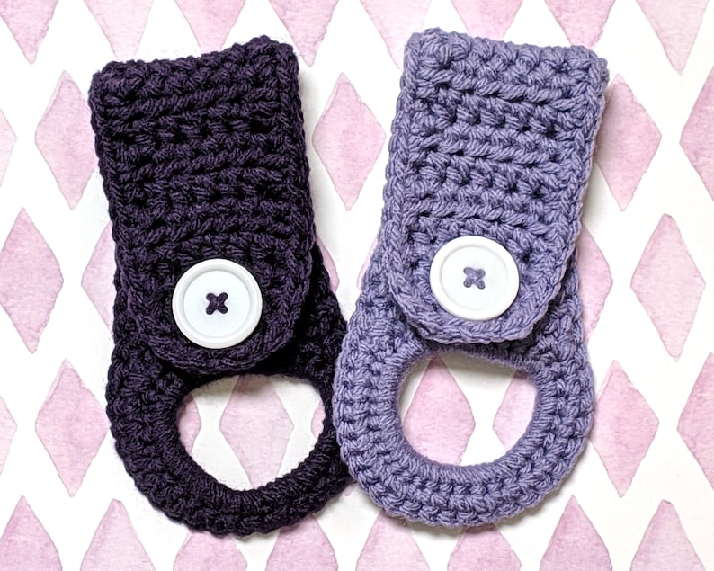 May include: Two crocheted towel holders with a button closure. One is dark purple and the other is light purple.