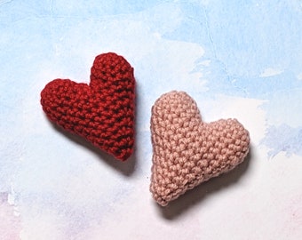 May include: Two crocheted hearts, one red and one pink, on a light blue background.