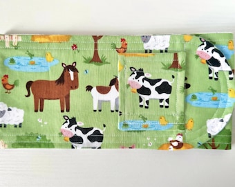 May include: Green fabric with a farm animal print. The fabric features cows, horses, chickens, and sheep. The fabric is sewn into a pocket with a curved edge.
