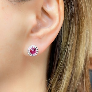 Può includere: Un paio di orecchini d'argento con un centro di cristallo rosa. Gli orecchini hanno un design delicato e intricato attorno al cristallo.