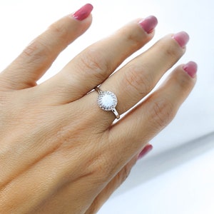 May include: A silver ring featuring a white opal stone encircled by smaller clear stones.