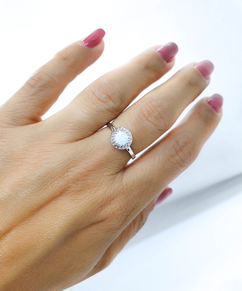 May include: A silver ring featuring a white opal stone encircled by smaller clear stones.