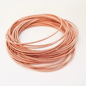 May include: A close-up of a bundle of rose gold coloured wire, coiled into a circle shape. The wire is thin and has a slightly textured surface.