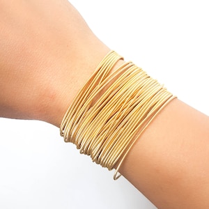 K&ouml;nnte beinhalten: Ein goldfarbenes Armband aus mehreren d&uuml;nnen, miteinander verwobenen Metallb&auml;ndern.