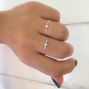 Puede incluir: Dos delicados anillos de cadena de plata con pequeños acentos de piedras preciosas. El anillo en el dedo índice tiene una piedra preciosa azul claro, mientras que el anillo en el dedo medio tiene una piedra preciosa rosa.