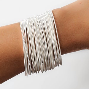 May include: A stack of silver bangle bracelets on a person's wrist. The bracelets are thin and delicate, and they are arranged in a neat and orderly fashion.