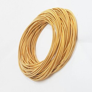 May include: A stack of gold-coloured metal bangles. The bangles are thin and have a slightly textured surface.