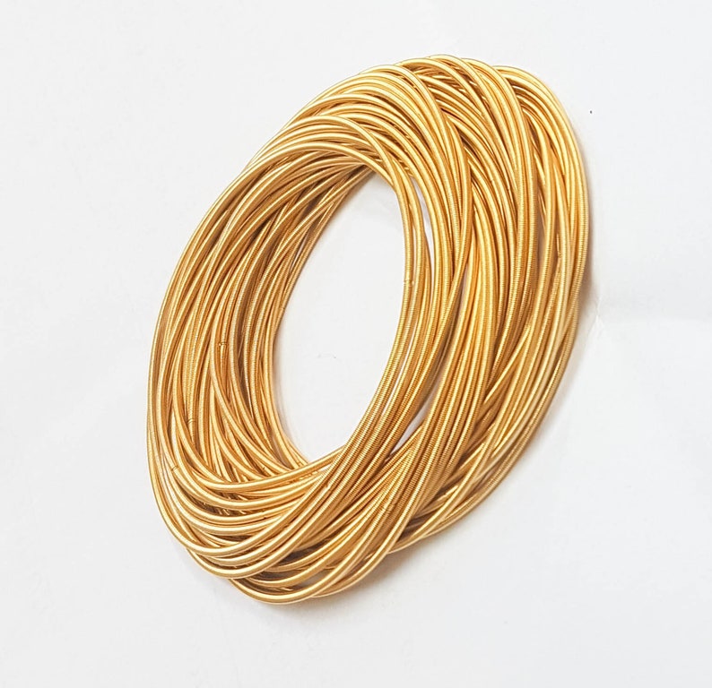 May include: A stack of gold-coloured metal bangles. The bangles are thin and have a slightly textured surface.