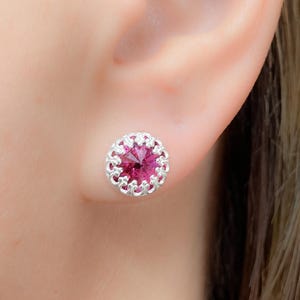 May include: A pair of silver earrings with a pink crystal center surrounded by a delicate filigree design.