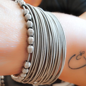 May include: A silver bracelet made of multiple strands of wire with silver beads. The bracelet is worn on a person's wrist.