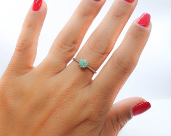 Op de afbeelding: Een zilveren ring met een ronde, lichtgroene edelsteen gezet in een zilveren bezel. De ring zit aan een vinger met rode nagellak.