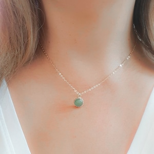 Op de afbeelding: Een delicate gouden ketting met een groene edelsteen hanger. De hanger is rond en heeft een getextureerde rand.