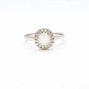 May include: A silver ring featuring a white opal stone set within a delicate, ornate halo.