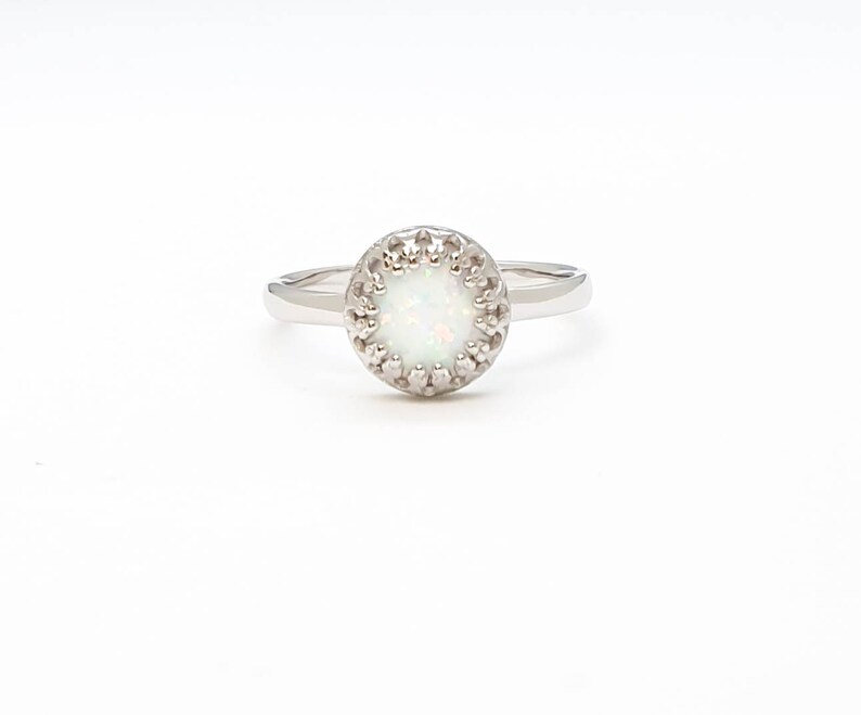 May include: A silver ring featuring a white opal stone set within a delicate, ornate halo.