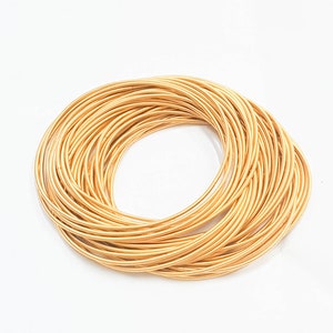 Pode incluir: Uma pilha de pulseiras de metal douradas. As pulseiras estão dispostas em círculo, com as pontas de cada pulseira sobrepostas.