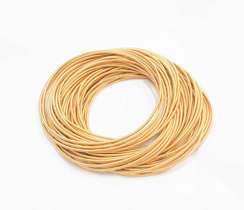 May include: A stack of gold-coloured metal bangles. The bangles are arranged in a circle, with the ends of each bangle overlapping the next.