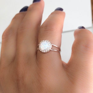May include: A silver ring with a white opal stone surrounded by smaller white stones.