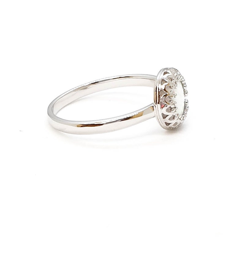 May include: A silver ring featuring a white oval stone set within an ornate filigree design.