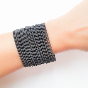 Puede incluir: Un brazalete de goma negro hecho de múltiples bandas delgadas apiladas una encima de la otra.