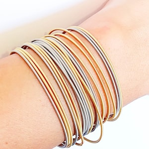 May include: A stack of gold and silver bangle bracelets on a person's wrist.