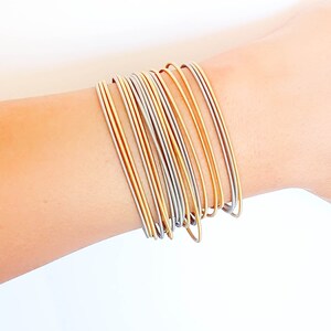 Peut inclure: Une collection de bracelets fins, dorés et argentés empilés sur un poignet. Les bracelets sont en métal et ont une finition lisse et brillante. Les bracelets dorés alternent avec des bracelets argentés, créant un effet bicolore. Les bijoux sont simples et élégants.