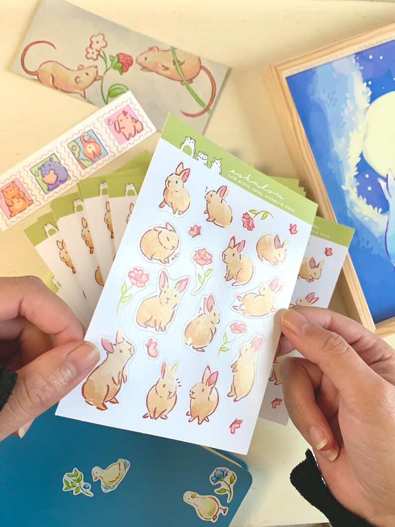 May include: A sheet of stickers featuring cute bunny illustrations with pink flowers and butterflies. The stickers are on a white background and have a green border. The text "toki no mori" is printed on the sheet, which translates to "forest of time".
