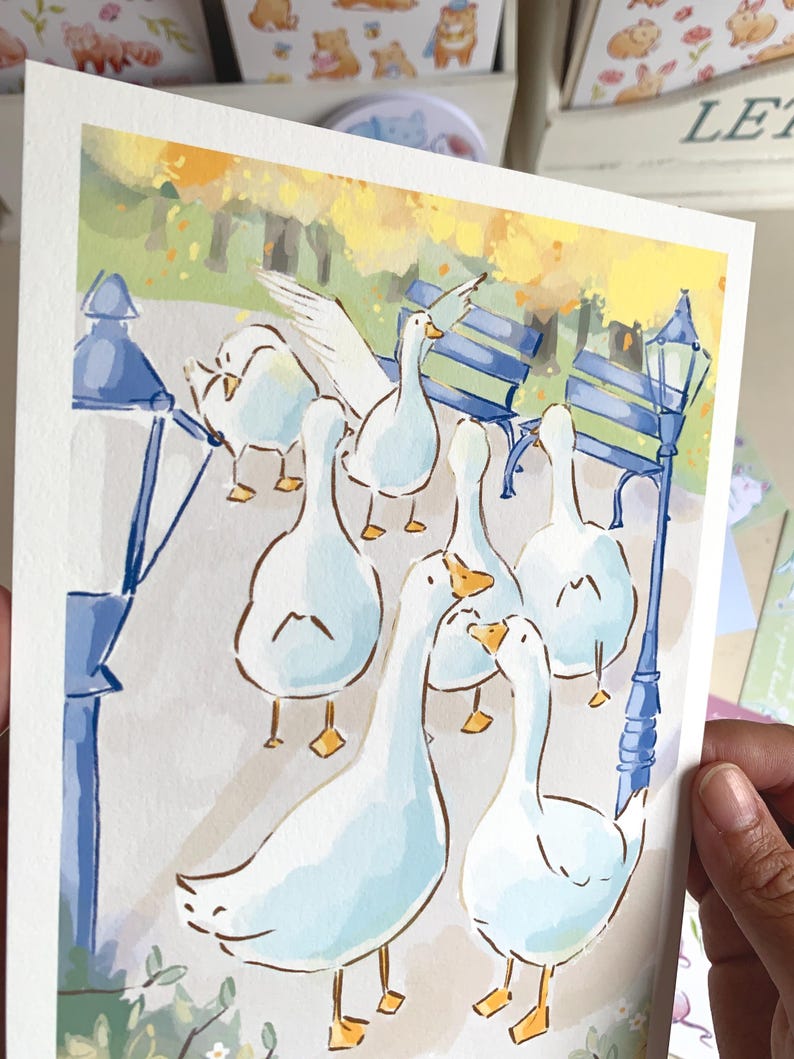 May include: Watercolor illustration of a flock of white geese in a park setting. The artwork features a soft color palette with blue, yellow, and green hues. The geese are depicted with detailed features, standing near a park bench and a lamppost.