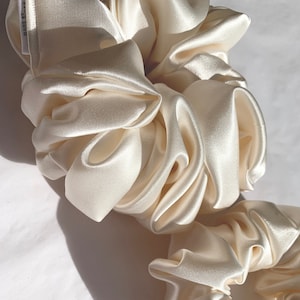 May include: Two ivory satin scrunchies, one larger than the other, with the text "MADE IN USA" on the larger scrunchie.
