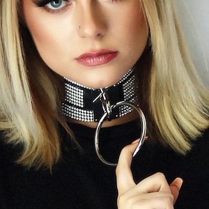 Può includere: Una donna con i capelli biondi indossa una maglietta nera e un choker argentato con strass.