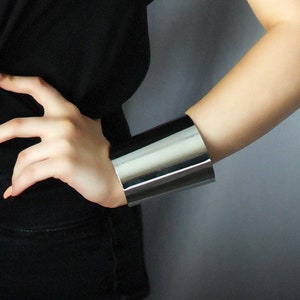 May include: A woman wearing a black t-shirt and black jeans with two silver metal cuff bracelets on her wrists.