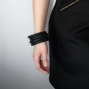 May include: A woman wearing a black sleeveless dress with a zipper detail on the side. She is wearing multiple black bracelets on her wrist.