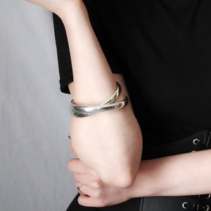 May include: A woman wearing a black t-shirt with a black corset belt. She has long brown hair with bangs and is wearing a silver bracelet on her left wrist.