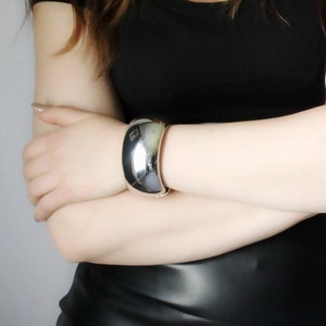 May include: A woman wearing a black top and a black leather skirt. She is wearing a silver bracelet on her left wrist.