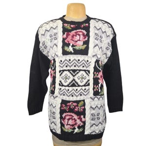 May include: A black sweater with a patchwork design featuring floral and geometric patterns. The sweater has long sleeves and a crew neck. The floral patches include pink roses and green leaves, with white and grey accents.