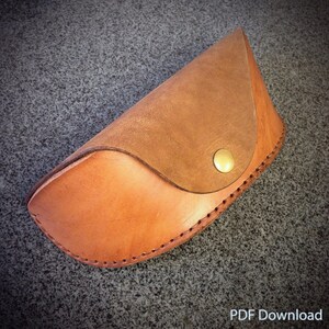 May include: A brown leather glasses case with a gold button closure. The case is stitched around the edges.